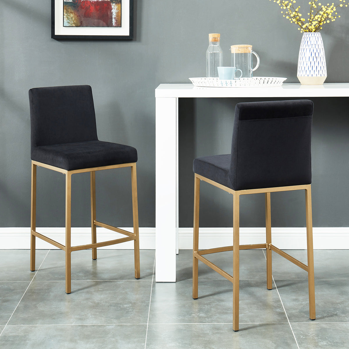 Staged lifestyle photo of two Diego 26-inch counter stools in black velvet with aged gold legs at a white table